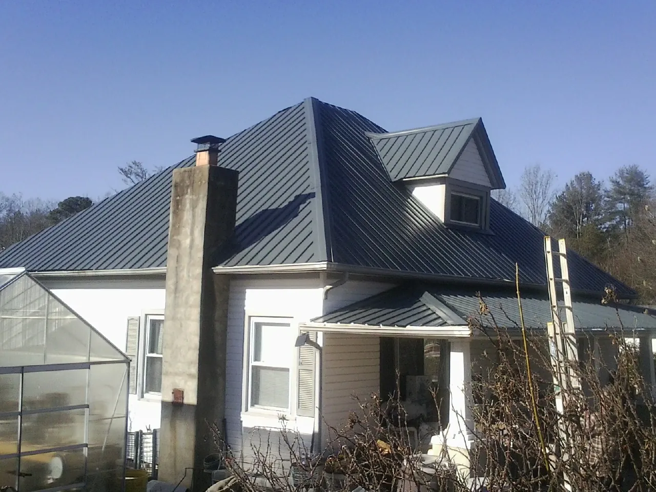 Dark blue standing seam metal roof on a white farmhouse with dormer — Slate & Tile Roof Repair by Roofing Brothers in Wadsworth
