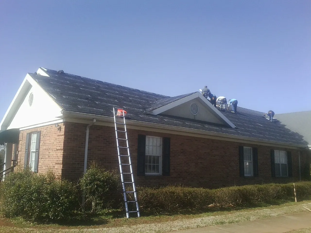 Crew tearing shingles off a brick ranch roof with a ladder set — Metal Roof Repair work by our crew in Wadsworth