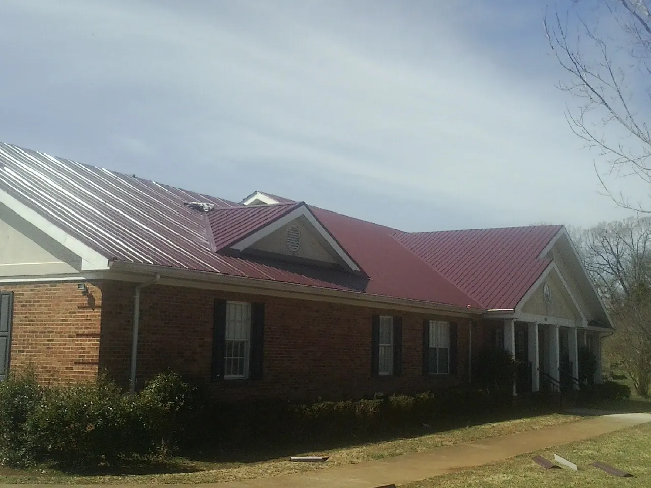 Red metal roof with gabled entries on a long brick building, from a Hail Damage Roof Repair job in Wadsworth