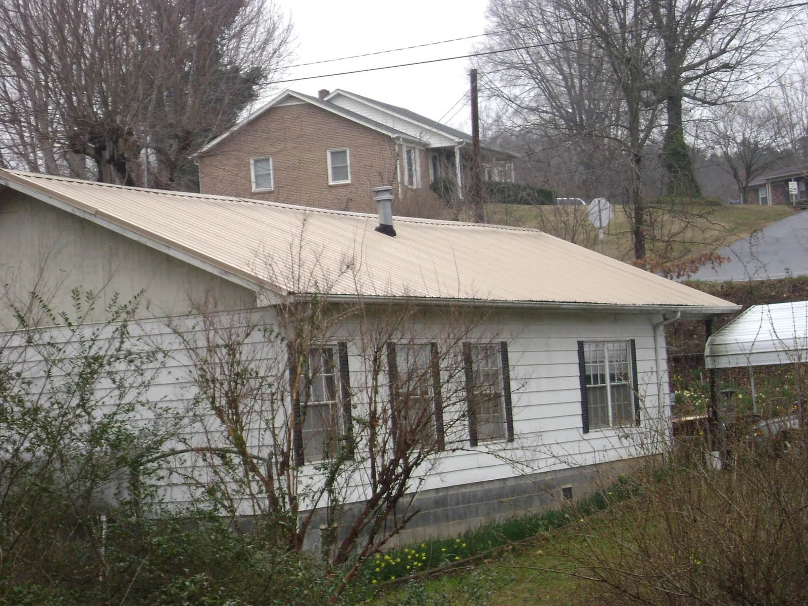 Tan metal roof on a white sided house set into a hillside — Commercial Roofing by Roofing Brothers in Wadsworth